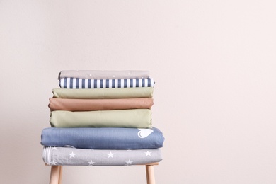 Photo of Stack of clean bed sheets on stool near beige wall. Space for text