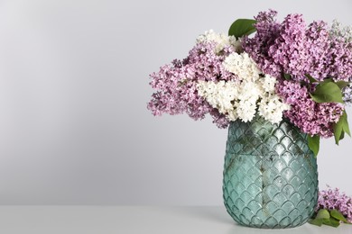 Beautiful lilac flowers in glass vase on light background. Space for text