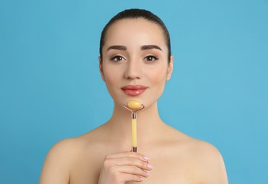 Photo of Woman using natural jade face roller on light blue background