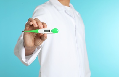 Male doctor holding digital thermometer on color background, closeup. Medical object