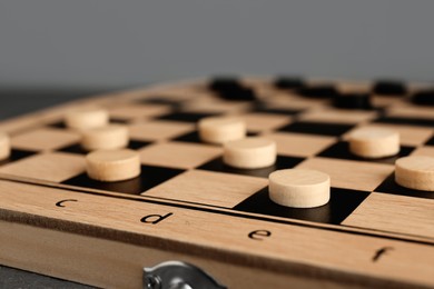 Photo of Wooden checkerboard with game pieces on light grey background, closeup