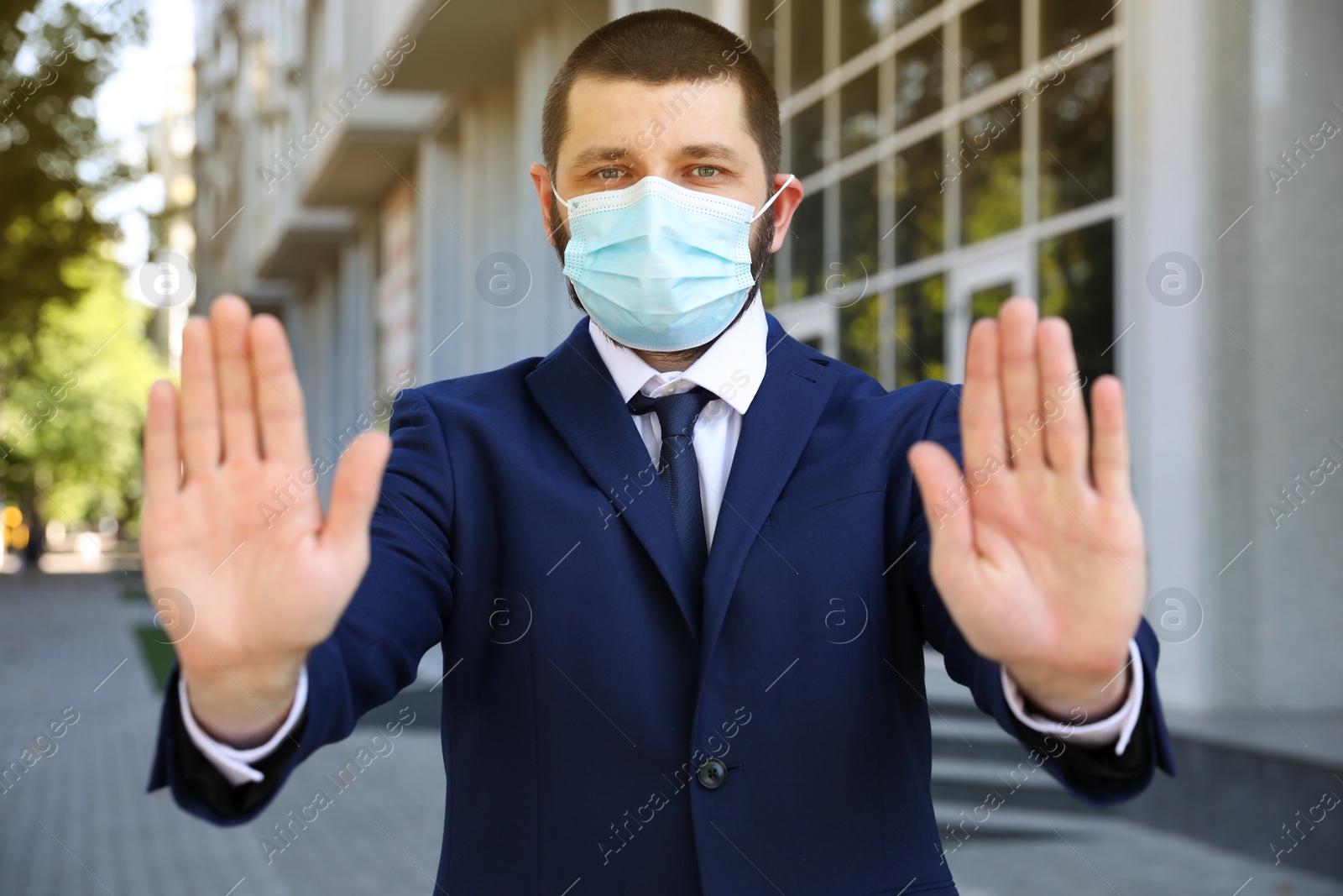 Photo of Man in protective face mask showing stop gesture outdoors. Prevent spreading of coronavirus