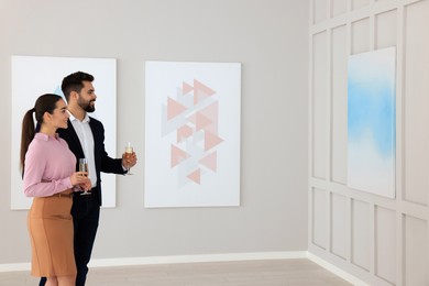 Photo of Young couple with glasses of champagne at exhibition in art gallery