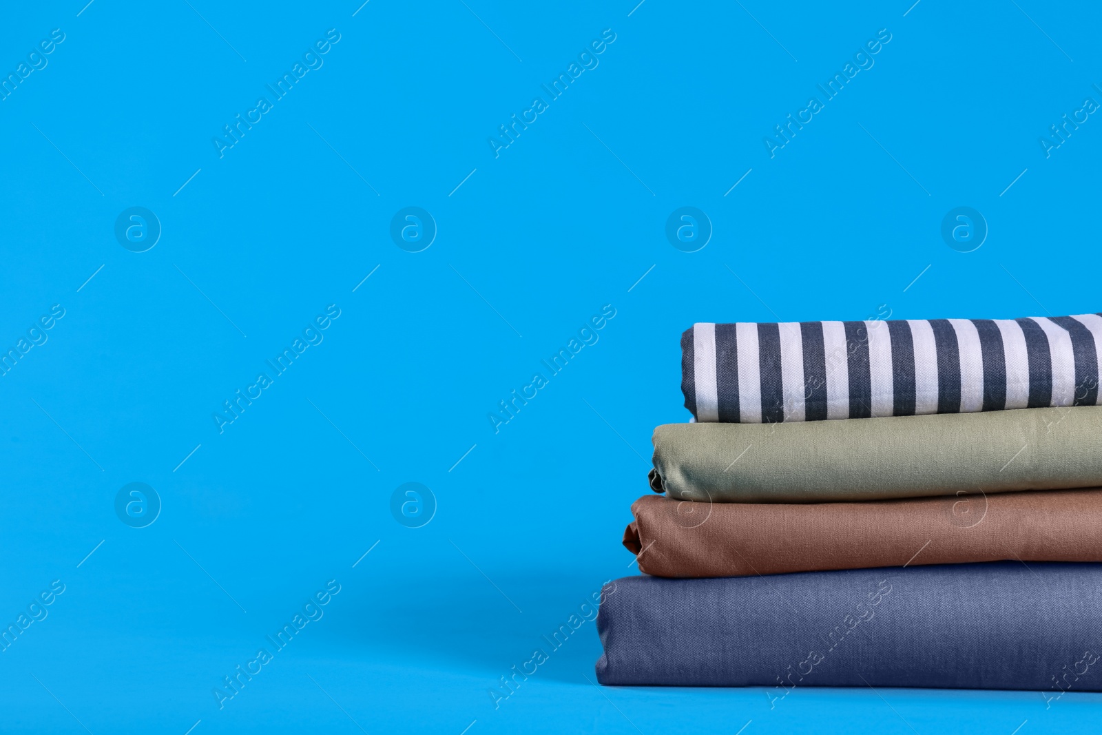 Photo of Stack of clean bed sheets on blue background. Space for text