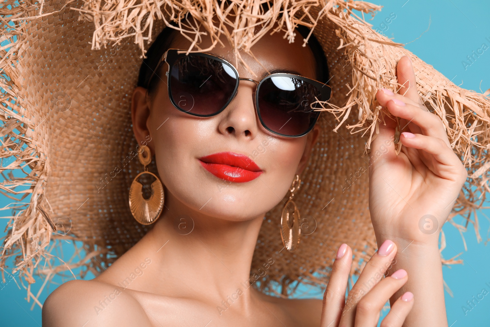 Photo of Attractive woman in fashionable sunglasses and wicker hat against light blue background, closeup