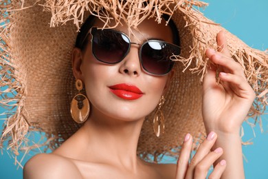 Photo of Attractive woman in fashionable sunglasses and wicker hat against light blue background, closeup