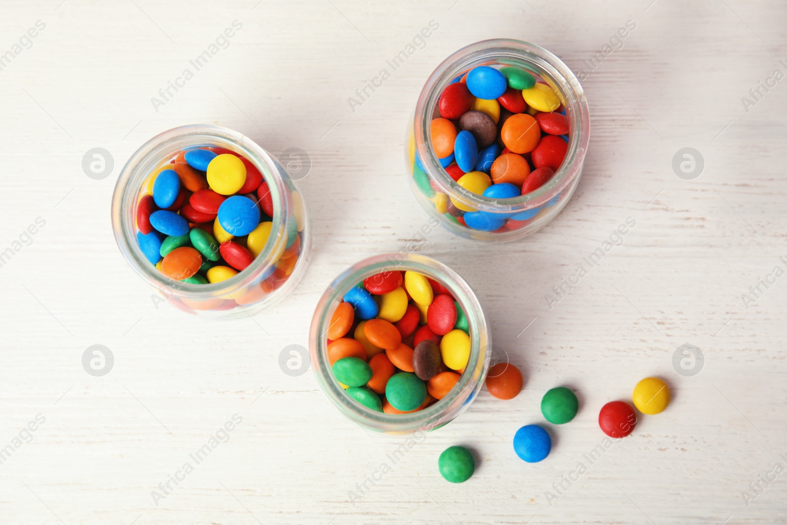 Photo of Jars with colorful candies on white wooden background, top view