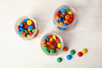 Jars with colorful candies on white wooden background, top view