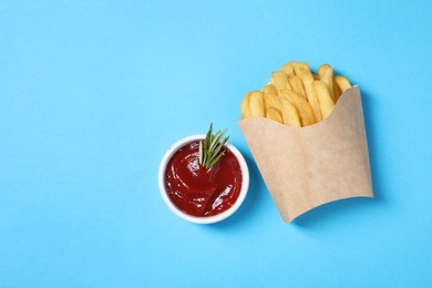 Photo of Paper cup with French fries, rosemary and ketchup on light blue table, flat lay. Space for text