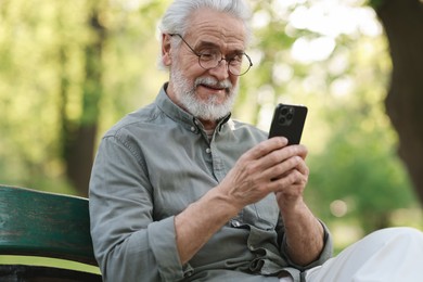 Photo of Portrait of happy grandpa with glasses using smartphone on bench in park