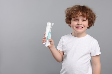 Photo of Cute little boy holding electric toothbrush and tube of toothpaste on light grey background, space for text