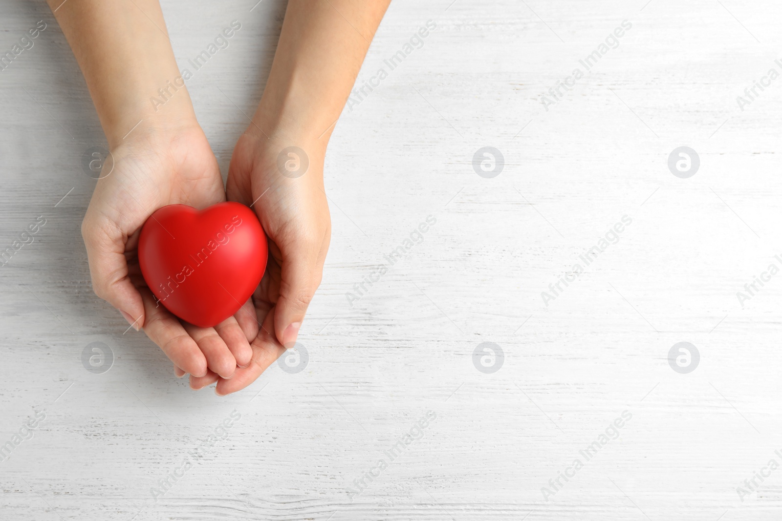 Photo of Woman holding red heart on wooden background, top view with space for text. Cardiology concept
