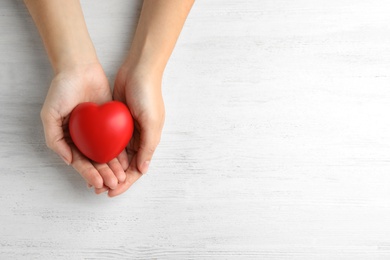 Woman holding red heart on wooden background, top view with space for text. Cardiology concept