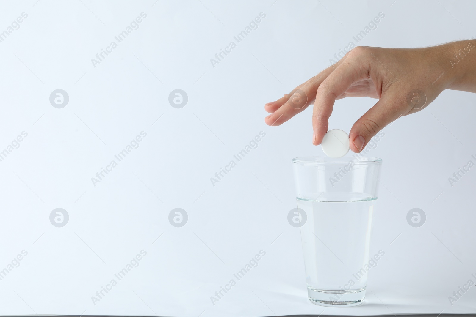 Photo of Woman putting tablet into glass of water on white background, space for text