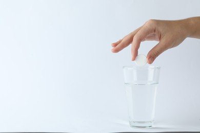 Woman putting tablet into glass of water on white background, space for text