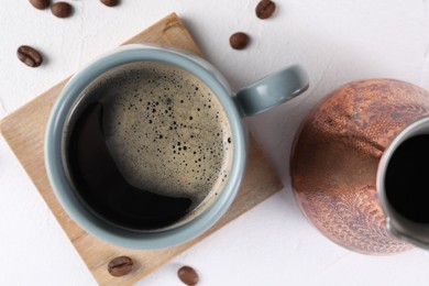 Photo of Delicious coffee in cup, cezve and beans on white textured table, flat lay