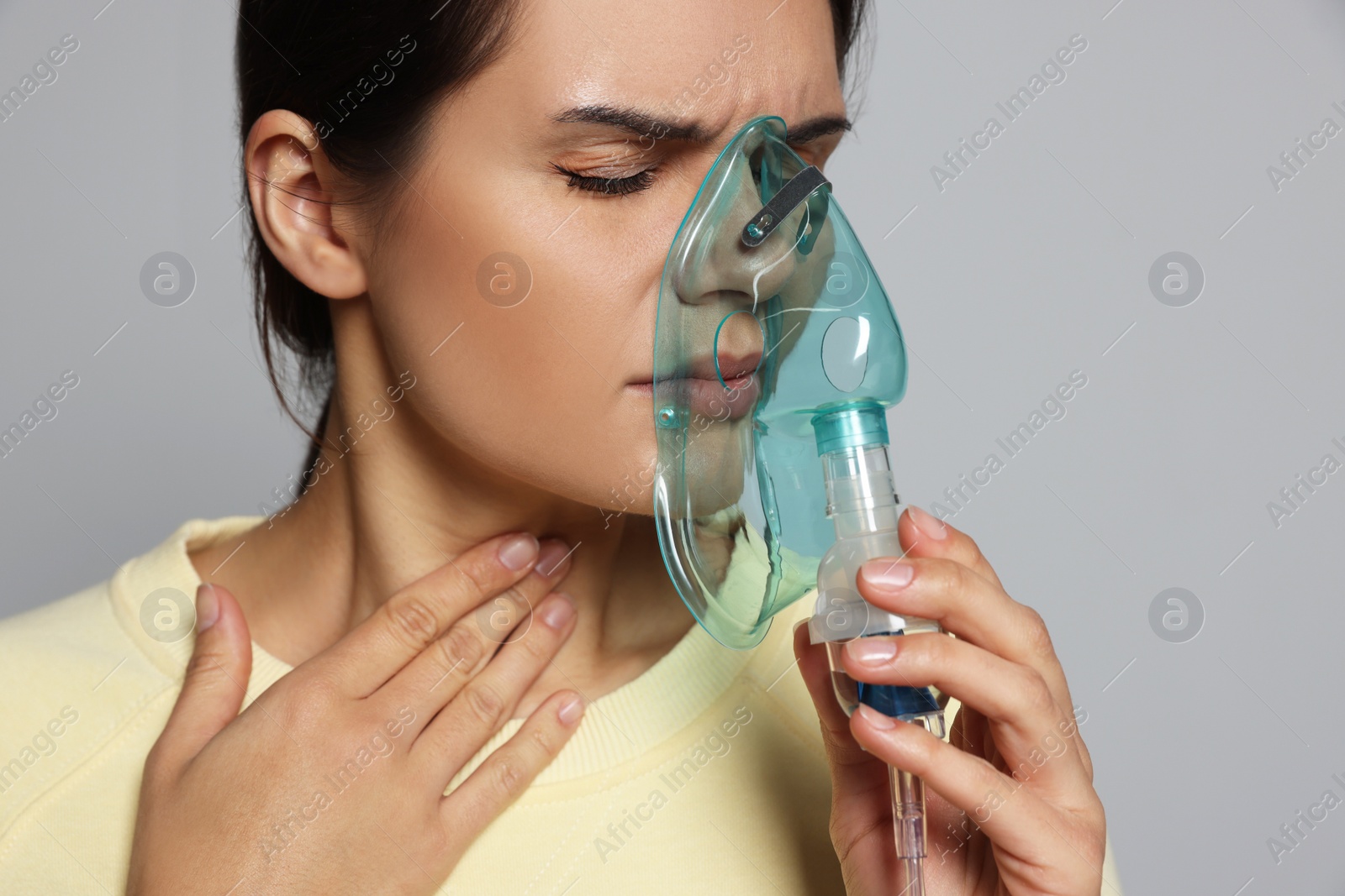 Photo of Sick young woman using nebulizer on grey background, closeup. Space for text