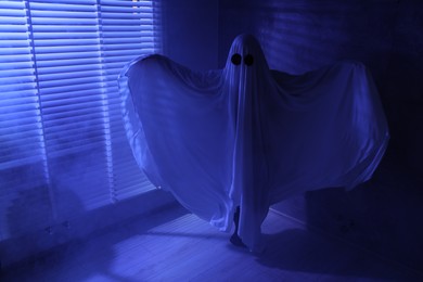 Photo of Creepy ghost. Woman covered with sheet near window in blue light