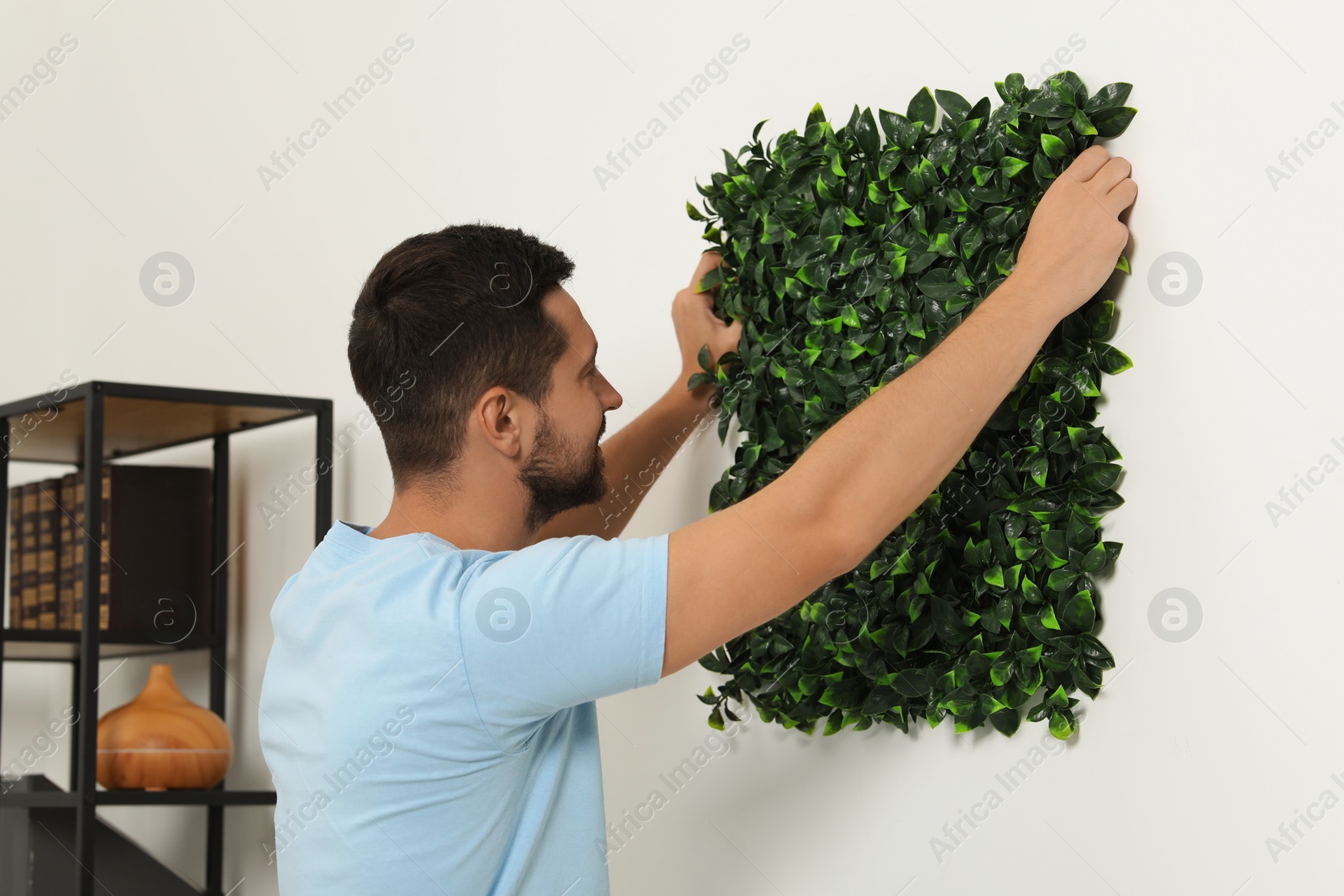 Photo of Man installing green artificial plant panel on white wall in room