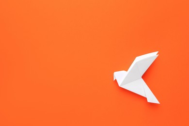 Photo of Beautiful white origami bird on orange background, top view. Space for text