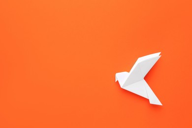 Beautiful white origami bird on orange background, top view. Space for text