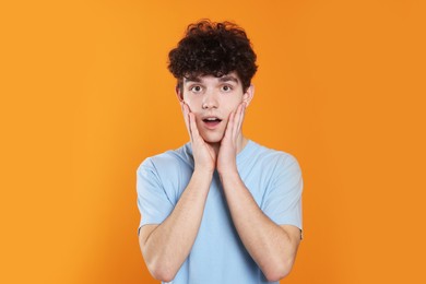 Portrait of shocked teenage boy on orange background