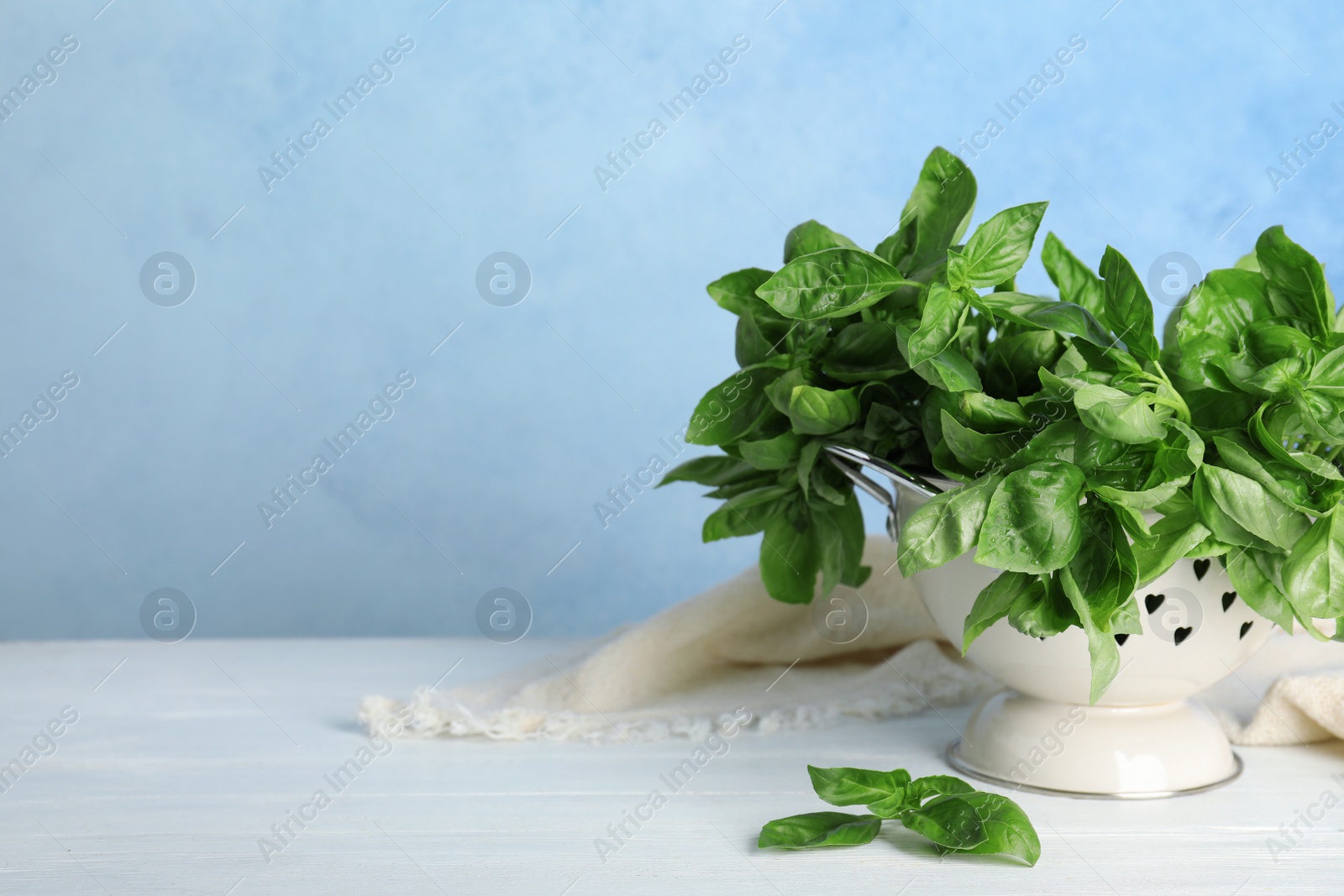 Photo of Colander with basil leaves on table against color background. Space for text