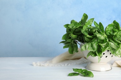 Colander with basil leaves on table against color background. Space for text