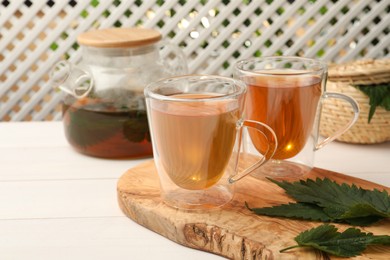 Aromatic nettle tea and green leaves on white wooden table, space for text