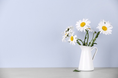 Photo of Beautiful tender chamomile flowers in jug on table against light background, space for text