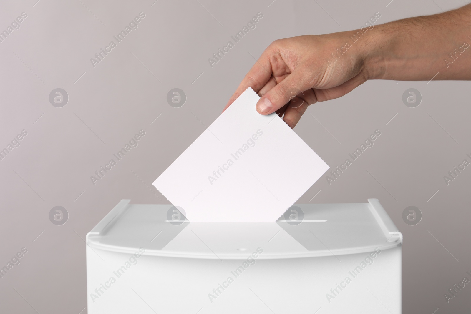 Photo of Man putting his vote into ballot box on light grey background, closeup