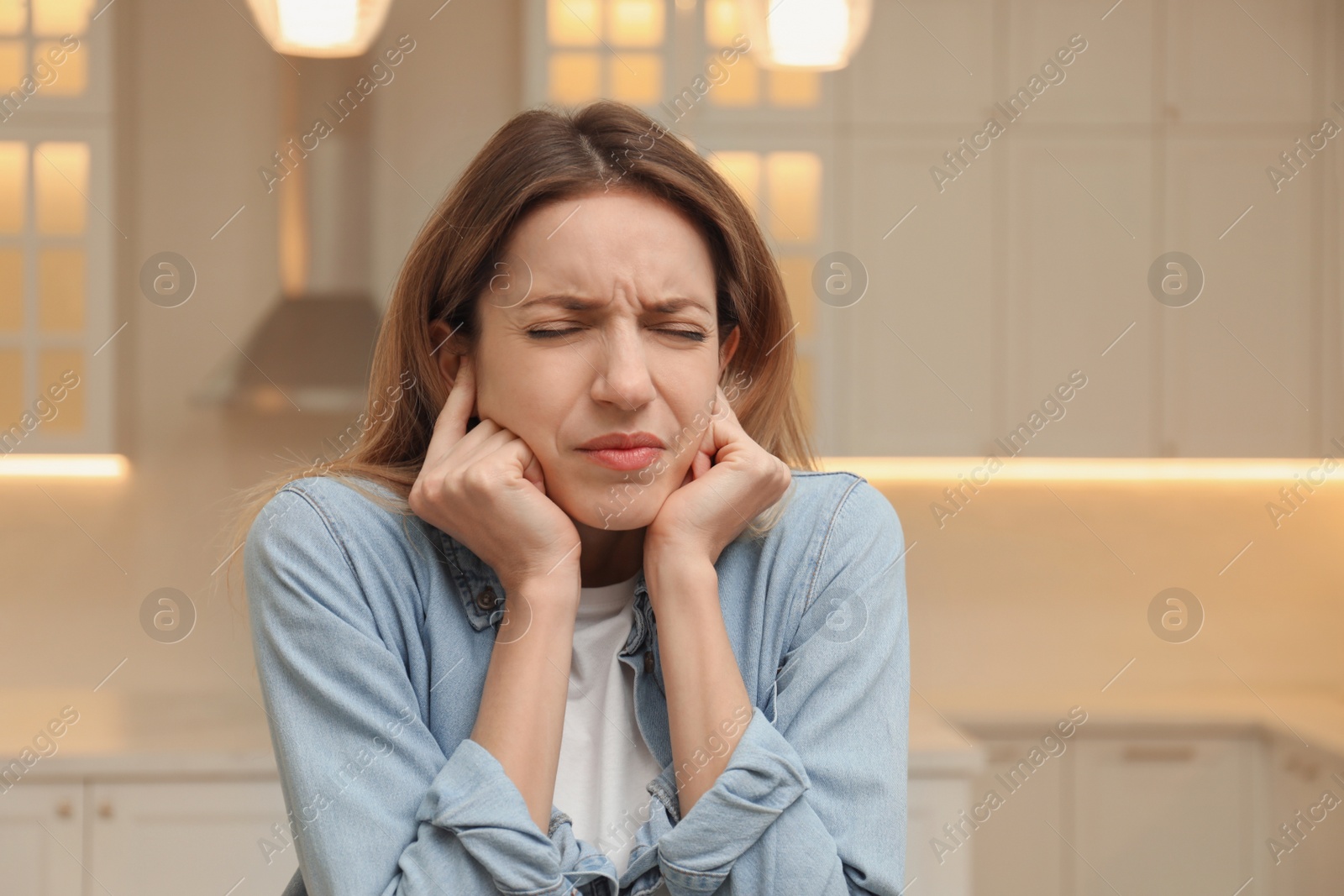 Photo of Emotional young woman covering her ears with fingers at home