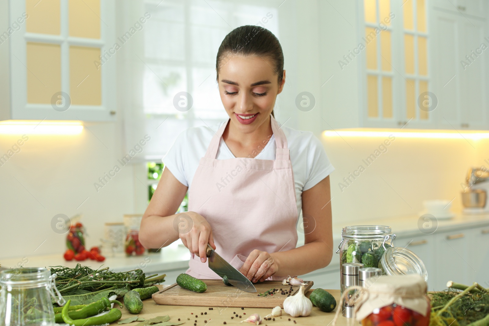 Photo of Woman cutting cucumber at table in kitchen. Preparing pickles