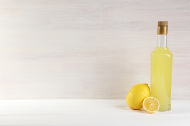 Photo of Bottle of tasty limoncello liqueur and lemons on white wooden table, space for text