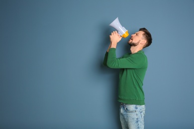 Photo of Young man shouting into megaphone on color background