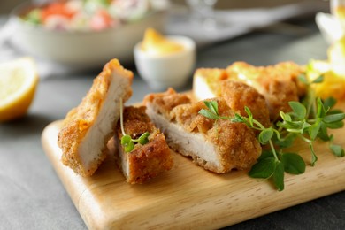 Photo of Delicious cut schnitzel served with microgreens on grey table, closeup