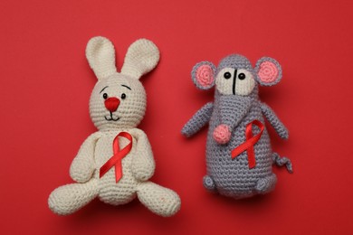 Photo of Cute knitted toys with ribbons on red background, top view. AIDS disease awareness