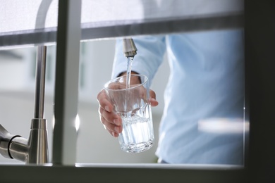 Photo of Man pouring water into glass in kitchen, closeup