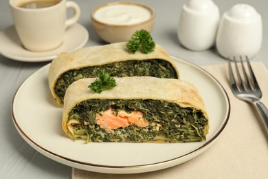 Photo of Pieces of delicious strudel with salmon and spinach on light grey table, closeup