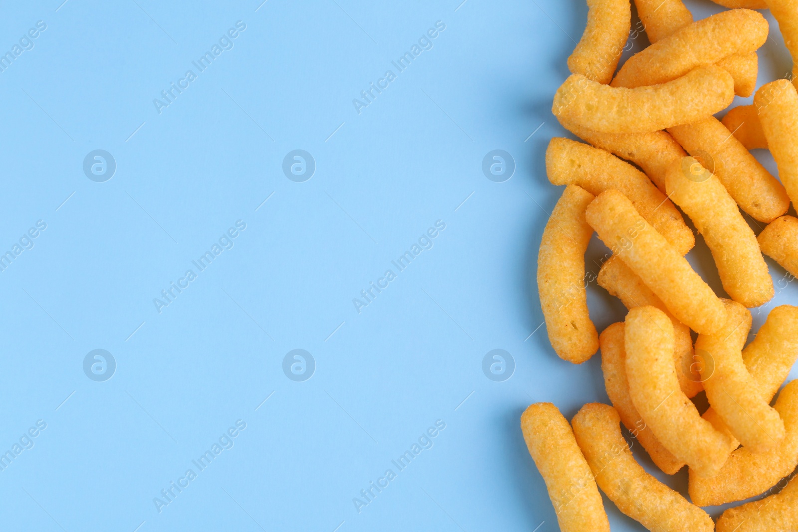 Photo of Heap of tasty cheesy corn puffs on light blue background, flat lay. Space for text