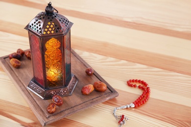 Photo of Muslim lantern Fanous, dried dates and prayer beads on wooden table. Space for text