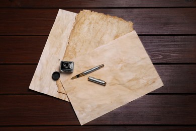 Photo of Inkwell, fountain pen and vintage parchment on wooden table, flat lay