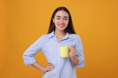 Photo of Happy young woman holding yellow ceramic mug on orange background
