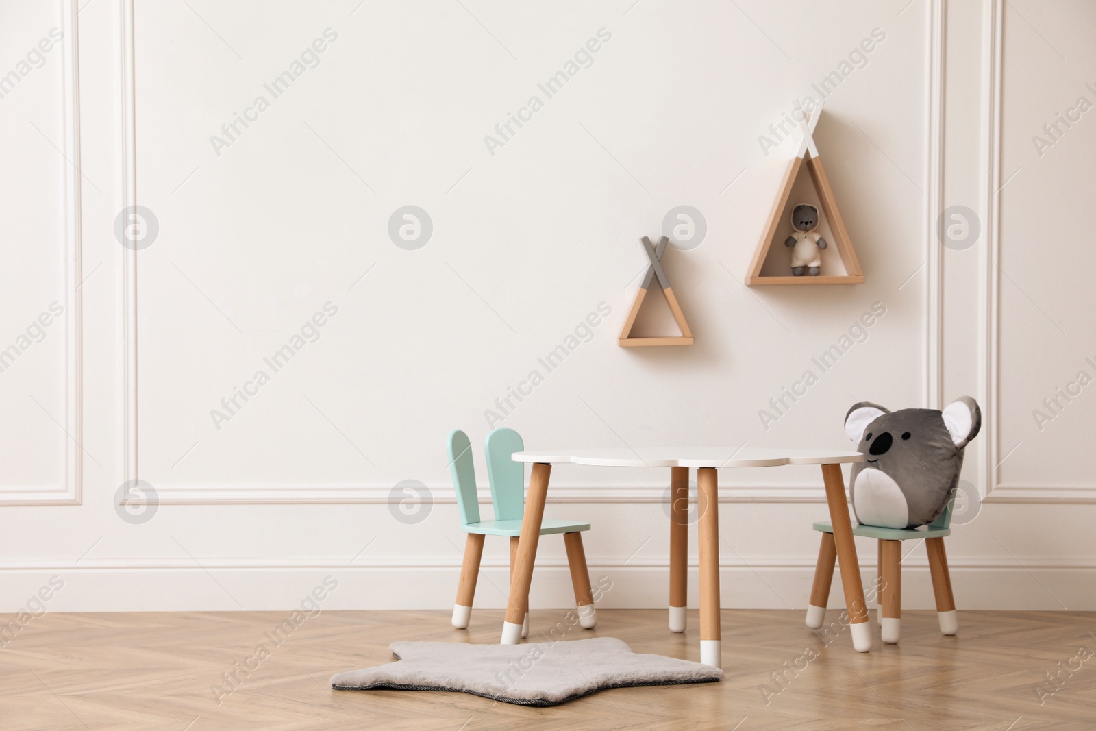 Photo of Cute child room interior with furniture, toys and wigwam shaped shelves on white wall. Space for text