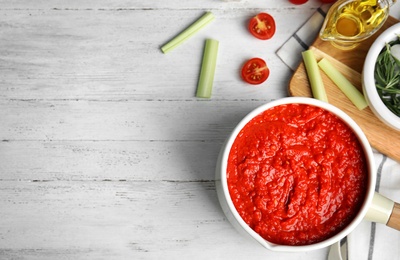 Photo of Flat lay composition with pan of tomato sauce on white wooden table, flat lay. Space for text