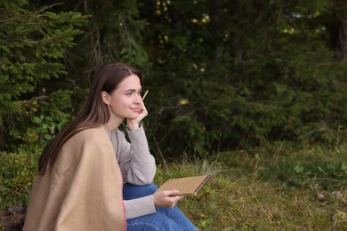 Photo of Young woman drawing with pencil in sketchbook near forest, space for text