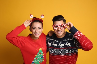 Photo of Couple in Christmas sweaters, Santa headband and party glasses on yellow background