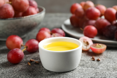 Photo of Bowl of natural grape seed oil on grey table. Organic cosmetic