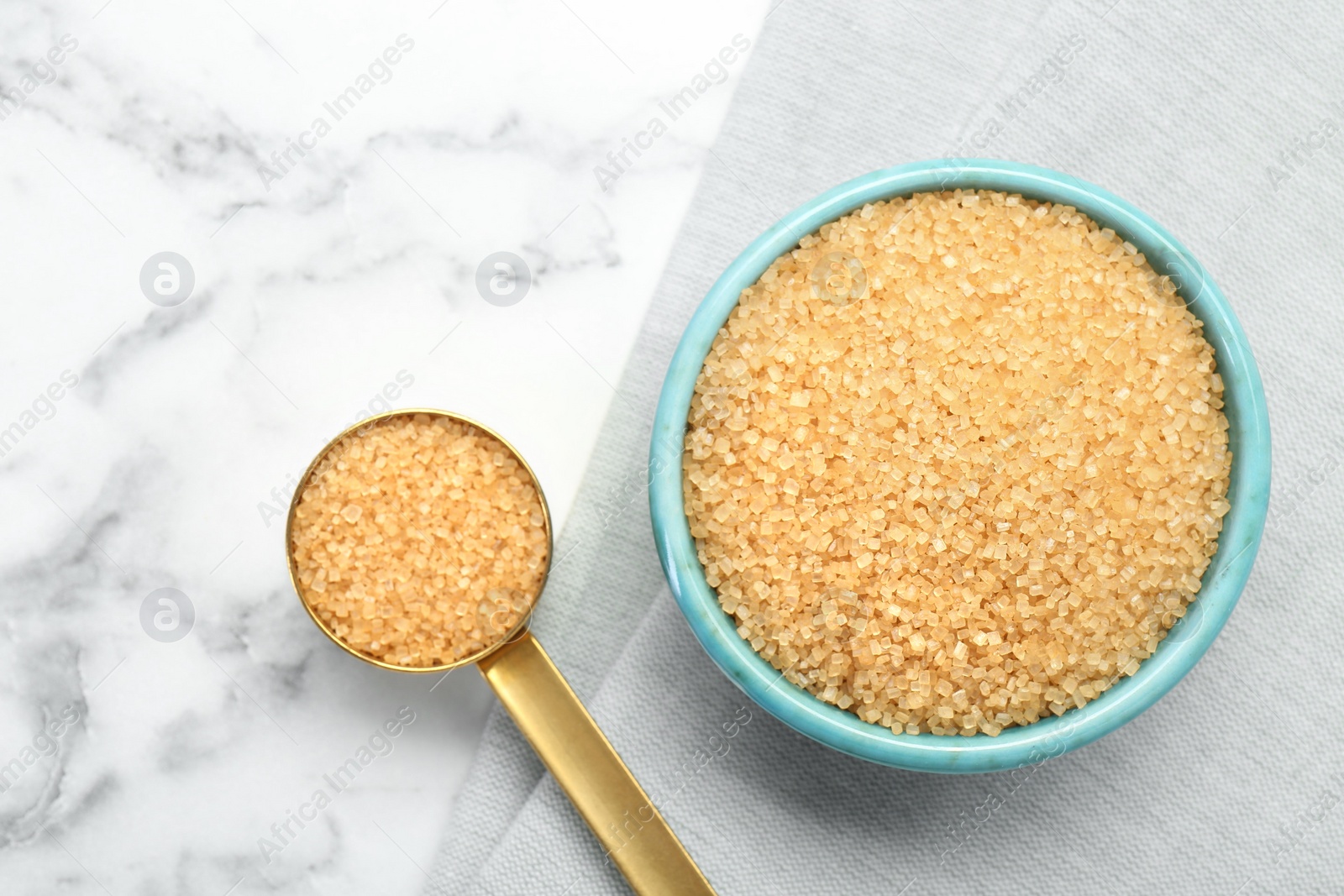 Photo of Brown sugar in bowl and scoop on white marble table, top view