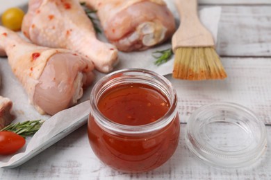 Photo of Marinade, basting brush and raw chicken drumsticks on white wooden table, closeup
